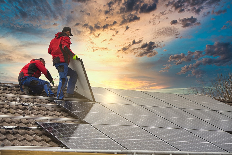 Two professionals installing residential solar panels on a tiled roof at sunset
