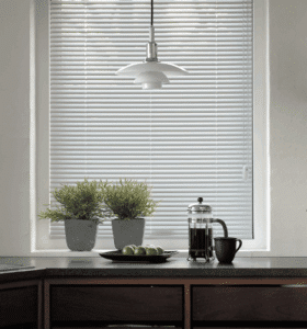 White aluminium Venetian blinds on a kitchen window with plants and coffee set
