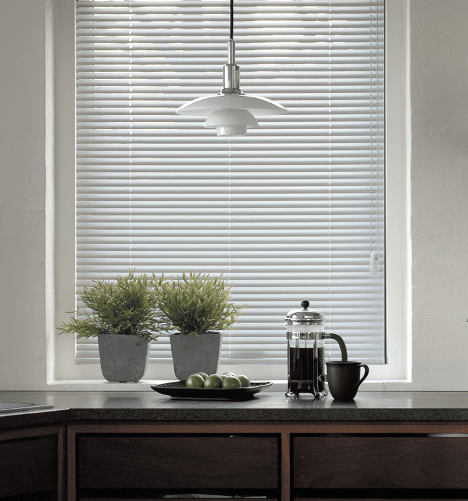 White aluminium Venetian blinds on a kitchen window with plants and coffee set