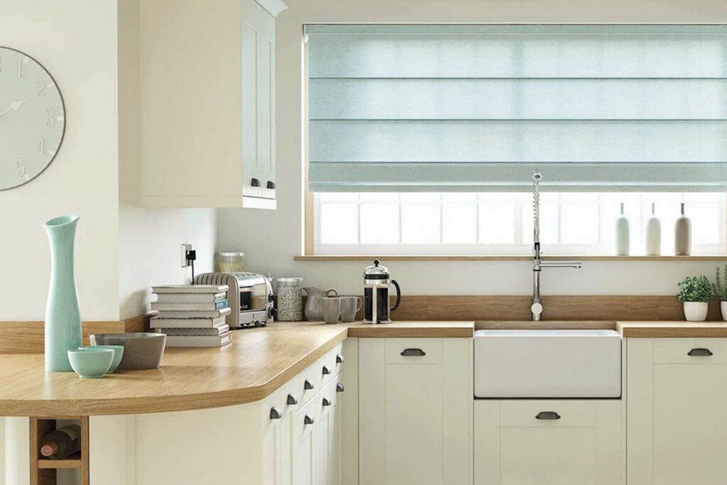 Roman blinds in Adelaide kitchen – light blue fabric blinds above farmhouse sink with white cabinets and wooden benchtops.